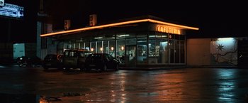 Movie still from “The Bourne Ultimatum” (2007), directed by Paul Greengrass – A restaurant with a neon sign and cars parked in front of it at night; Extreme Wide shot, Low angle