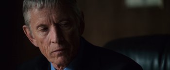 Movie still from “The Bourne Ultimatum” (2007), directed by Paul Greengrass – An older man wearing a blue shirt and a blue jacket; Close Up shot, Over the shoulder angle