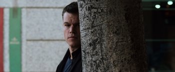 Movie still from “The Bourne Ultimatum” (2007), directed by Paul Greengrass – A person leaning against a tree trunk; Close Up shot, Low angle
