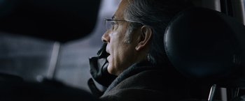 Movie still from “The Bourne Ultimatum” (2007), directed by Paul Greengrass – An older man wearing glasses is sitting in a car; Close Up shot, Over the shoulder angle