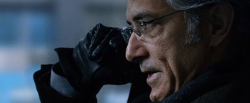 Movie still from “The Bourne Ultimatum” (2007), directed by Paul Greengrass – An older man wearing glasses and a black leather glove; Close Up shot, Low angle