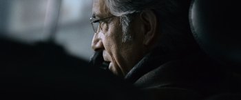 Movie still from “The Bourne Ultimatum” (2007), directed by Paul Greengrass – An older man wearing glasses looking off into the distance; Close Up shot, Over the shoulder angle