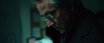 Movie still from “The Bourne Ultimatum” (2007), directed by Paul Greengrass – An older man wearing glasses looking down at something; Close Up shot, Low angle
