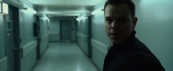 Movie still from “The Bourne Ultimatum” (2007), directed by Paul Greengrass – A man standing in a dark hallway with lights on; Close Up shot, Low angle