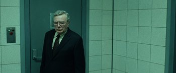 Movie still from “The Bourne Ultimatum” (2007), directed by Paul Greengrass – An older man wearing a suit and tie standing next to a wall; Medium shot, Low angle