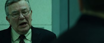 Movie still from “The Bourne Ultimatum” (2007), directed by Paul Greengrass – A man in a suit and tie sitting in front of a wall; Close Up shot, Over the shoulder angle