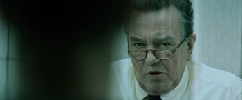 Movie still from “The Bourne Ultimatum” (2007), directed by Paul Greengrass – An older man wearing glasses and a white shirt; Close Up shot, Over the shoulder angle