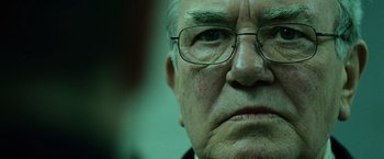 Movie still from “The Bourne Ultimatum” (2007), directed by Paul Greengrass – An older man wearing glasses looking at the camera; Close Up shot, Over the shoulder angle