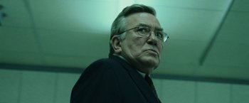 Movie still from “The Bourne Ultimatum” (2007), directed by Paul Greengrass – An older man wearing glasses and a suit and tie; Close Up shot, Low angle