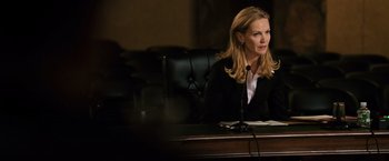 Movie still from “The Bourne Ultimatum” (2007), directed by Paul Greengrass – A woman sitting at a table in front of a microphone; Medium shot, Over the shoulder angle