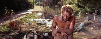 Movie still from “The Bridge on the River Kwai” (1957), directed by David Lean – A shirtless man in the woods holding onto a pole; Medium shot, High angle