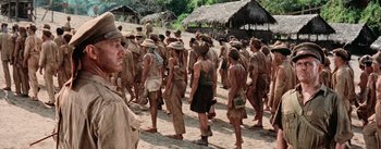 Movie still from “The Bridge on the River Kwai” (1957), directed by David Lean – A large group of people are gathered together in the dirt; Medium shot, High angle