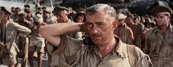 Movie still from “The Bridge on the River Kwai” (1957), directed by David Lean – An older man in a military uniform with his hands behind his head; Close Up shot, Low angle