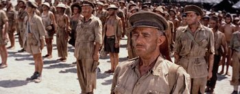 Movie still from “The Bridge on the River Kwai” (1957), directed by David Lean – A large group of men in uniform standing next to each other on a beach; Medium shot, Low angle