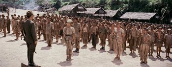 Movie still from “The Bridge on the River Kwai” (1957), directed by David Lean – A large group of men in uniform standing in a field; Wide shot, High angle