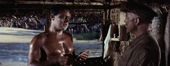 Movie still from “The Bridge on the River Kwai” (1957), directed by David Lean – A shirtless man in the rain is brushing his teeth in the shower; Medium shot, Low angle