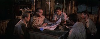 Movie still from “The Bridge on the River Kwai” (1957), directed by David Lean – A group of men sitting at a table looking at papers; Medium shot, High angle