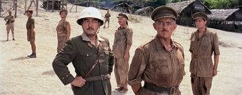 Movie still from “The Bridge on the River Kwai” (1957), directed by David Lean – A group of men standing next to each other on top of a dirt field; Medium shot, Low angle