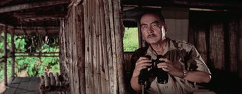 Movie still from “The Bridge on the River Kwai” (1957), directed by David Lean – An older man holding a pair of binoculars in his hand; Medium shot, Low angle