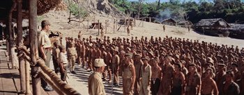 Movie still from “The Bridge on the River Kwai” (1957), directed by David Lean – A large group of men standing next to each other on a dirt field; Extreme Wide shot, High angle