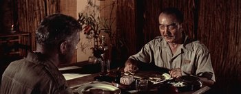 Movie still from “The Bridge on the River Kwai” (1957), directed by David Lean – A man sitting at a table with a plate of food in front of him; Medium shot, Over the shoulder angle