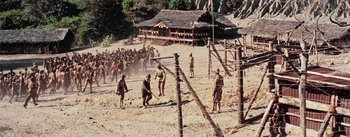 Movie still from “The Bridge on the River Kwai” (1957), directed by David Lean – A group of people in the sand near barbed wire fences; Extreme Wide shot, High angle