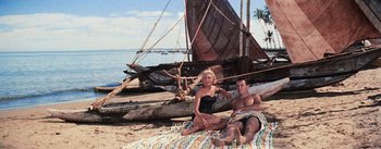 Movie still from “The Bridge on the River Kwai” (1957), directed by David Lean – A man and a woman sitting on a blanket on the beach; Wide shot, High angle