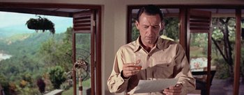 Movie still from “The Bridge on the River Kwai” (1957), directed by David Lean – A man holding a glass of wine while reading a paper; Medium shot, Low angle