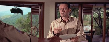 Movie still from “The Bridge on the River Kwai” (1957), directed by David Lean – A man holding a glass of beer while looking at a paper; Close Up shot, Over the shoulder angle