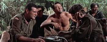 Movie still from “The Bridge on the River Kwai” (1957), directed by David Lean – A man sitting on the ground next to two other men; Medium shot, Low angle