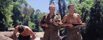 Movie still from “The Bridge on the River Kwai” (1957), directed by David Lean – A man holding a gun while standing next to two other men; Medium shot, Low angle