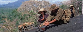 Movie still from “The Bridge on the River Kwai” (1957), directed by David Lean – A man and a woman putting on shoes on the roof of a house; Wide shot, Low angle