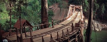 Movie still from “The Bridge on the River Kwai” (1957), directed by David Lean – A person standing on a wooden bridge over a river; Extreme Wide shot, High angle