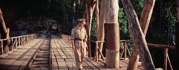 Movie still from “The Bridge on the River Kwai” (1957), directed by David Lean – A man walking across a bridge holding a cane; Wide shot, Low angle