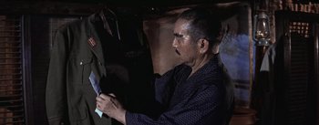 Movie still from “The Bridge on the River Kwai” (1957), directed by David Lean – An older man looking at something in his hand; Medium shot, Over the shoulder angle