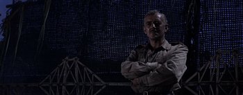 Movie still from “The Bridge on the River Kwai” (1957), directed by David Lean – A man standing with his arms crossed in front of a wall; Medium shot, Low angle