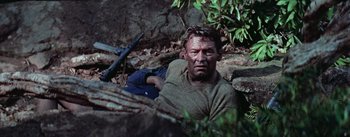 Movie still from “The Bridge on the River Kwai” (1957), directed by David Lean – A man laying on the ground in the woods; Medium shot, High angle
