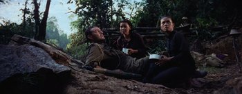 Movie still from “The Bridge on the River Kwai” (1957), directed by David Lean – A man and two women sitting on the ground; Medium shot, High angle