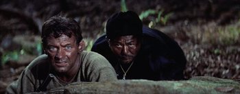Movie still from “The Bridge on the River Kwai” (1957), directed by David Lean – A man in a black hat is leaning on the ground; Close Up shot, Low angle