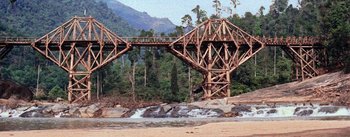 Movie still from “The Bridge on the River Kwai” (1957), directed by David Lean – A wooden bridge over a body of water near a forest; Extreme Wide shot, Low angle
