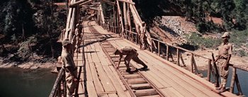 Movie still from “The Bridge on the River Kwai” (1957), directed by David Lean – A dog is standing on a wooden bridge; Wide shot, High angle