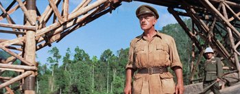 Movie still from “The Bridge on the River Kwai” (1957), directed by David Lean – A man in a military uniform standing under a wooden structure; Medium shot, Low angle