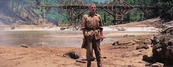 Movie still from “The Bridge on the River Kwai” (1957), directed by David Lean – A man standing next to a dead body on a beach; Wide shot, Low angle