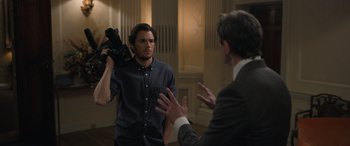 Movie still from “The Bubble” (2022), directed by Judd Apatow – A man holding a video camera in front of another man in a suit; Medium shot, Over the shoulder angle