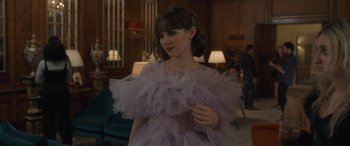 Movie still from “The Bubble” (2022), directed by Judd Apatow – A woman in a purple dress standing in front of a window; Medium shot, Over the shoulder angle