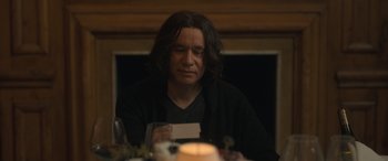 Movie still from “The Bubble” (2022), directed by Judd Apatow – A man sitting at a table holding a card; Close Up shot, Over the shoulder angle