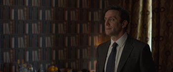 Movie still from “The Bubble” (2022), directed by Judd Apatow – A man wearing a suit and tie in front of bookshelves; Close Up shot, Over the shoulder angle