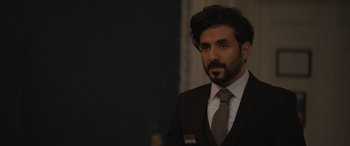 Movie still from “The Bubble” (2022), directed by Judd Apatow – A man wearing a suit and tie in front of a wall; Close Up shot, Over the shoulder angle