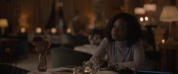 Movie still from “The Bubble” (2022), directed by Judd Apatow – A woman sitting at a table with a plate of food in front of her; Close Up shot, Over the shoulder angle