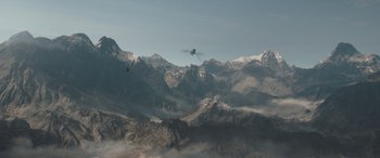 Movie still from “The Bubble” (2022), directed by Judd Apatow – A helicopter flying over a mountain range with clouds in the background; Extreme Wide shot, High angle